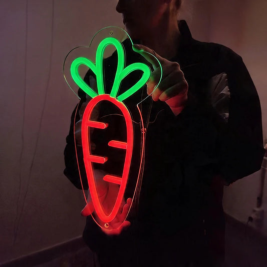 Person holding a neon sign shaped like a carrot with green top and red body.