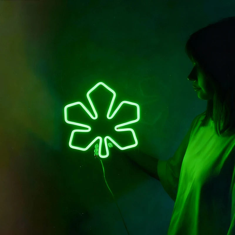 Person interacting with a glowing green neon sign shaped like a chestnut leaf on a dark background