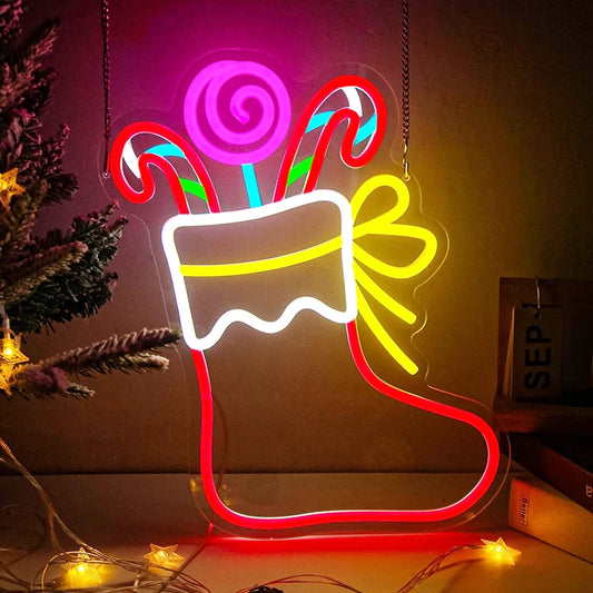 A glowing acrylic Christmas stocking LED neon sign with candy canes, a lollipop, and a bow, illuminated in multiple vibrant colors against a dark background.
