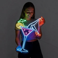 Person holding a neon sign of a cocktail glass with colorful lights on a dark background