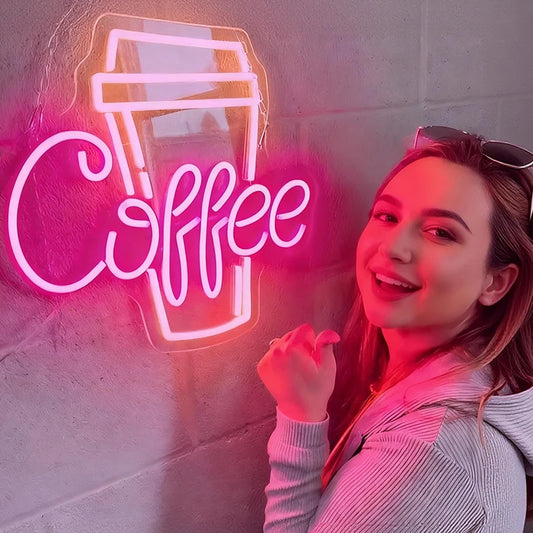 Woman posing in front of a neon 'Coffee' sign on a wall.