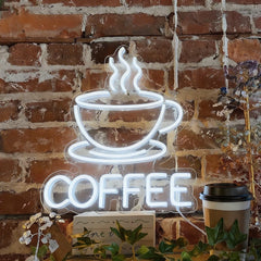 Neon sign of a white color coffee cup with steam against a brick wall, accompanied by a paper cup.