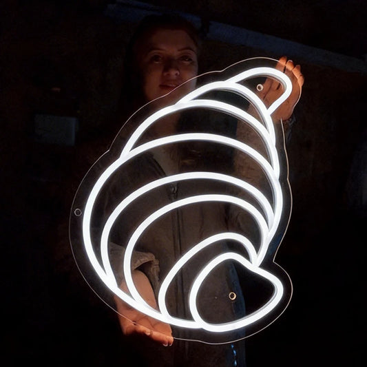 Person holding a neon white light shaped like a croissant in a dark setting