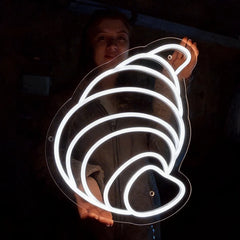 Person holding a neon white light shaped like a croissant in a dark setting