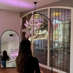 Woman in front of a neon sign with 'Just Married' and a cupid design, in a room with decorative mirrors and lighting.