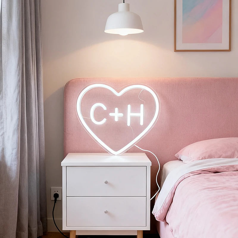 Neon sign in the shape of a heart with initials on a bed in a bedroom.