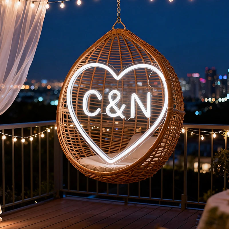 Wicker chair with neon heart and initials 'C&N' on a balcony at night.