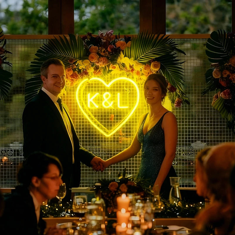 Two people shaking hands in front of a neon heart sign with 'K&L' in a celebratory setting.