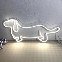 Neon white light shaped like a dachshund on a textured wall with small robot toys below.