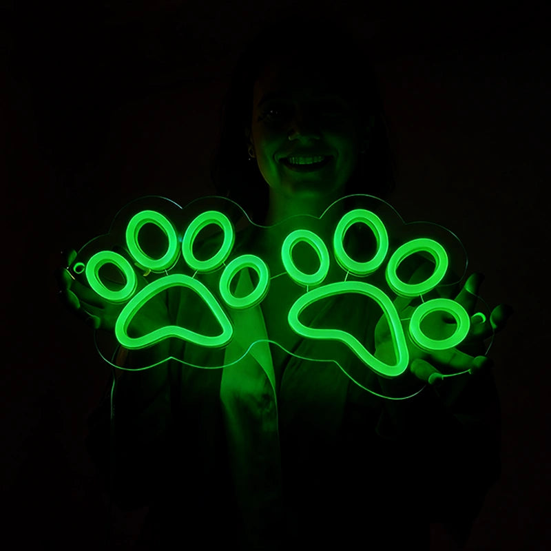 A woman holding a green neon sign with paw designs in a dark setting