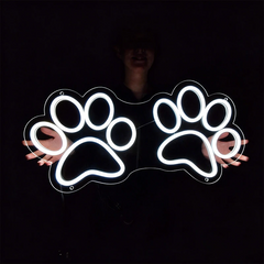 Neon sign shaped like a paw print held by two hands against a dark background