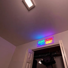 Neon sign on a wall with text 'DON'T OVER THINK SHIT' in a room.