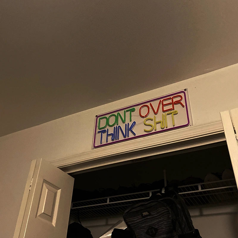 Colorful sign on a door with text 'DON'T OVER THINK SHIT' in a room.