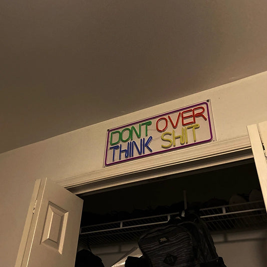 Colorful sign on a door with text 'DON'T OVER THINK SHIT' in a room.