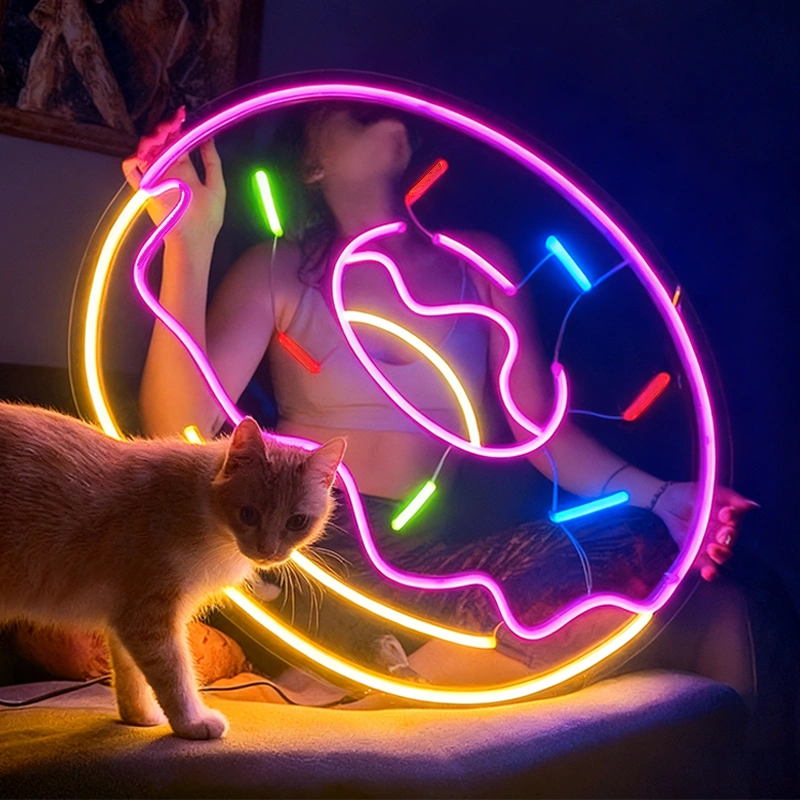 Person holding a colorful neon light donut with a cat.