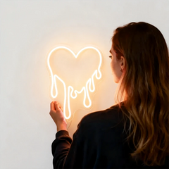 Person looking at a neon sign shaped like a heart on a plain background