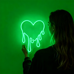 Person interacting with a glowing green heart-shaped neon sign against a solid green background