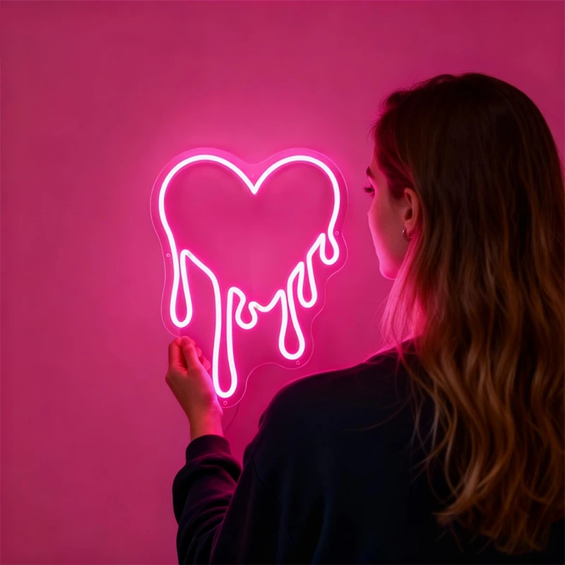 Person holding a pink neon sign shaped like a heart with the word 'love' on a pink background