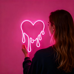 Person holding a pink neon sign shaped like a heart with the word 'love' on a pink background