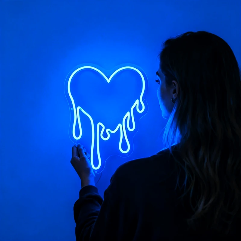 Person interacting with a neon sign shaped like a heart on a blue background