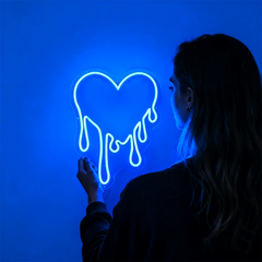 Person interacting with a neon sign shaped like a heart on a blue background