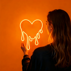 Person holding an orange dripping heart neon sign against a white background
