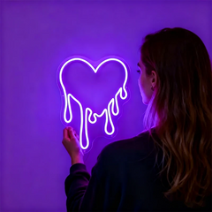 Person interacting with a neon sign shaped like a heart on a purple background