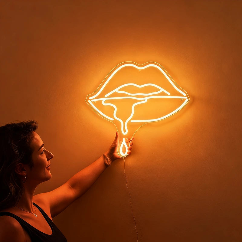 Woman holding a neon warm white sign shaped like lips against a wall.