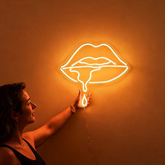 Woman holding a neon warm white sign shaped like lips against a wall.