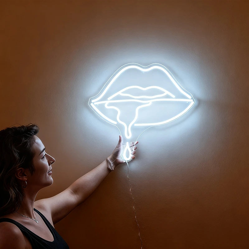 Woman holding a neon white sign shaped like lips against a wall.