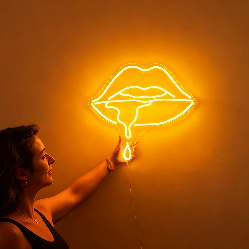 Woman holding a neon yellow sign shaped like lips against a wall.