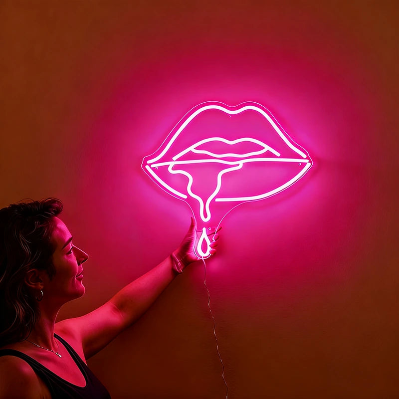 Woman holding a neon hot pink sign shaped like lips against a wall.