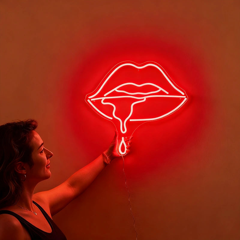 Woman holding a neon red sign shaped like lips against a wall.