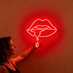 Woman holding a neon red sign shaped like lips against a wall.