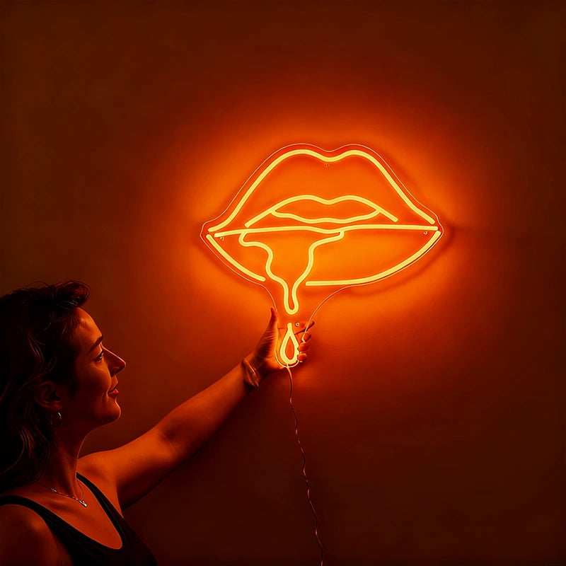 Woman holding a neon orange sign shaped like lips against a wall.