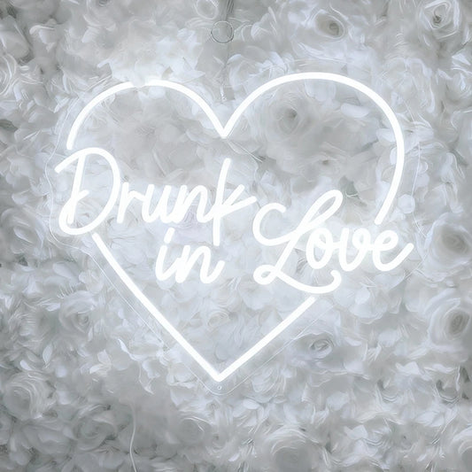 Neon white sign with 'Drunk in Love' text in the shape of a heart on a floral background