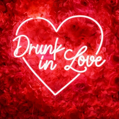 Neon red sign with 'Drunk in Love' text inside a heart shape on a red floral background