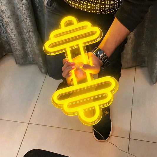 Person holding a lemon yellow neon sign shaped like a dumbbell on a tiled floor.