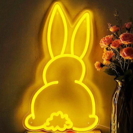 A glowing Easter bunny neon sign in lemon yellow leaning against the wall beside a flower.