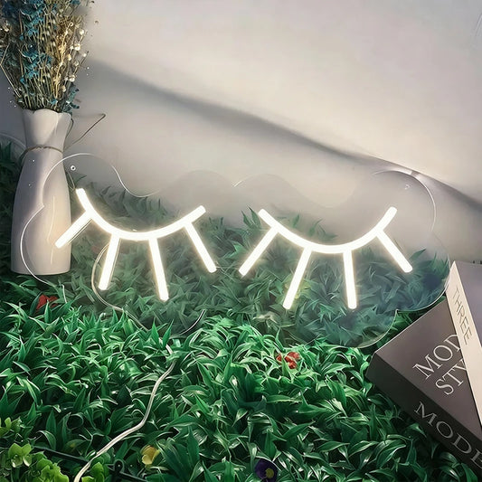 Neon eyelash lights on a grassy surface with a vase and book in the background