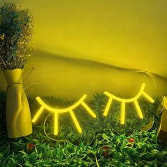 Neon eyelash lights on grass with a yellow background