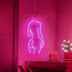 Neon sign of a hot pink woman's silhouette on a dark wall with a table and decorative lights.