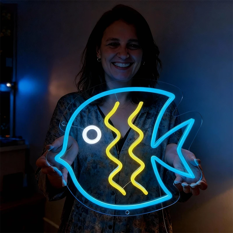 Person holding a neon sign shaped like a fish with ice blue, white and lemon yellow colors.