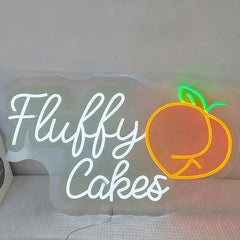 Neon sign with 'Fluffy Cakes' and a peach icon on a plain background