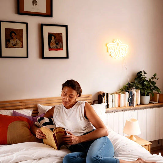 Woman reading a book on a bed in a cozy bedroom with warm white keith haring flying man neon sign on the wall.