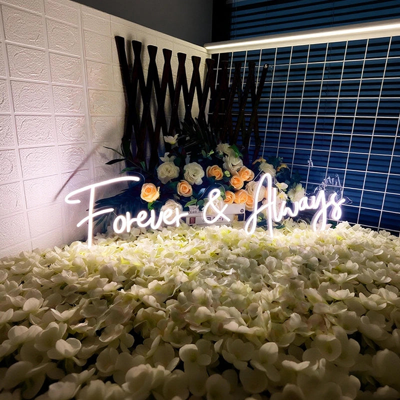 Neon sign reading 'Forever & Always' surrounded by flowers on a decorative stand.