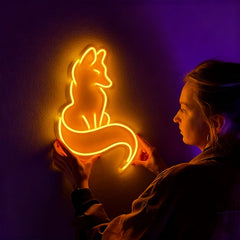 Person holding a glowing neon sign of a fox against a dark background