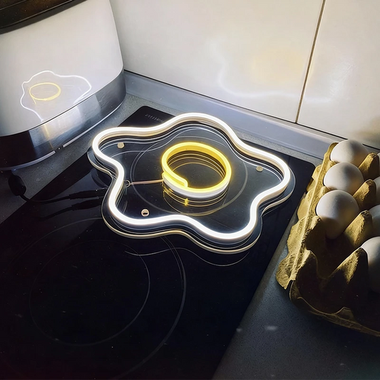 Neon light shaped like a fried egg on a stove with eggs in a carton nearby.