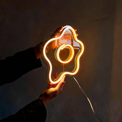 Neon light shaped like a fried egg held by a person against a dark background