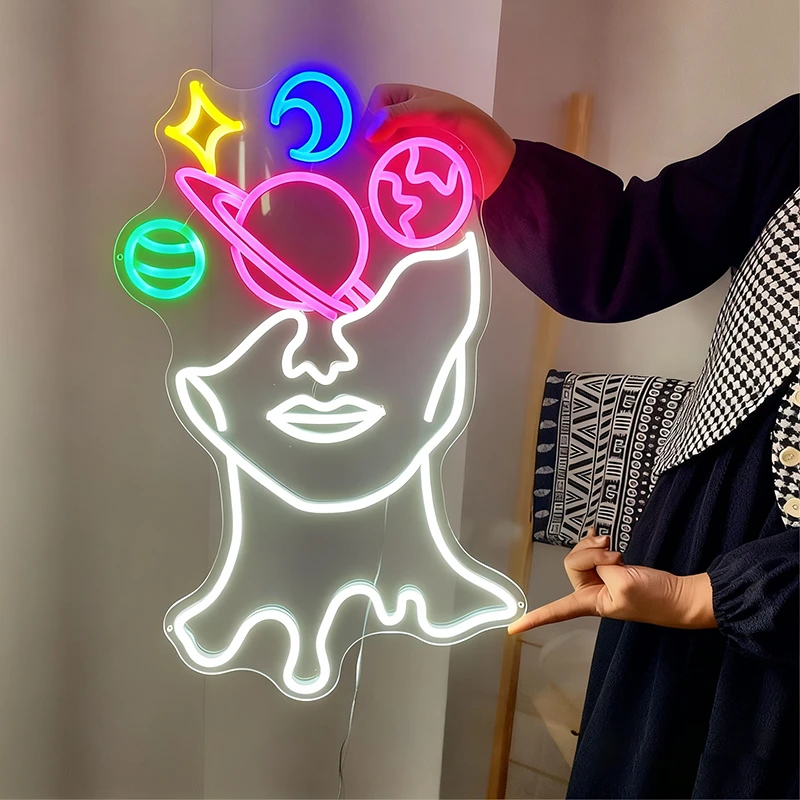 Neon light shaped like a face with colorful galaxy symbols in brain held by a person.